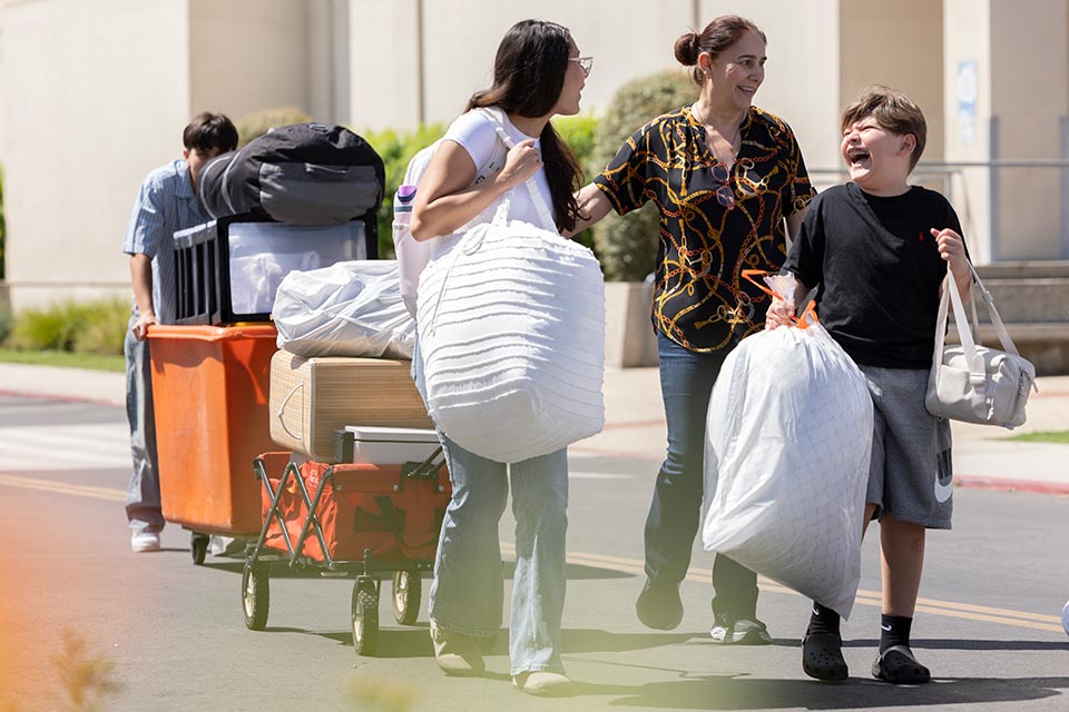 Student and her young sibling walking with a cart of housing items.