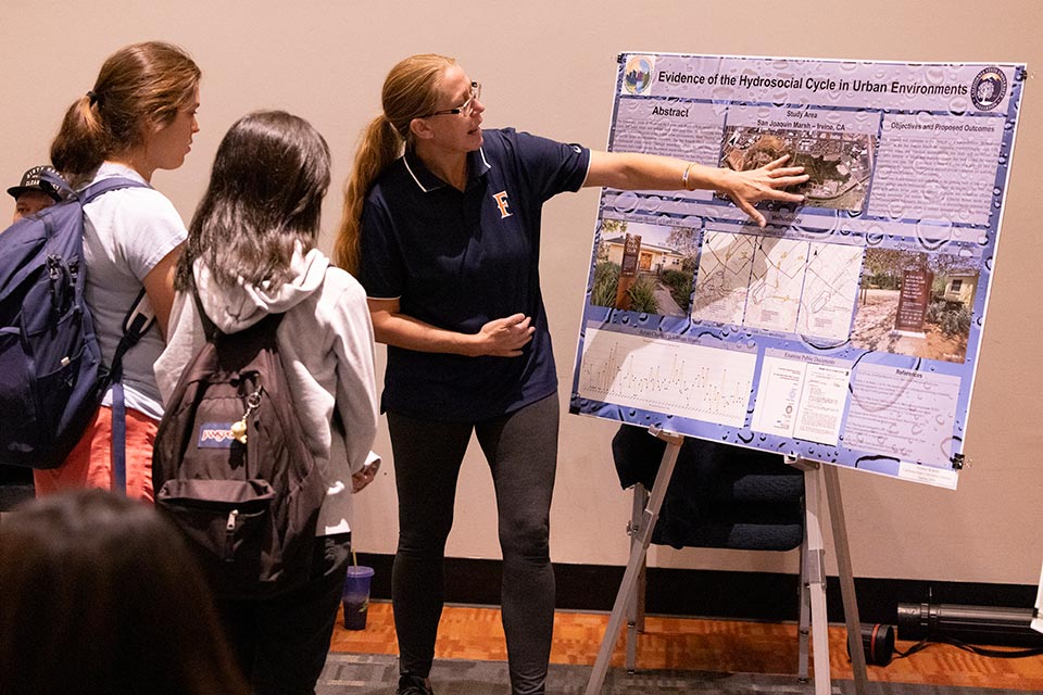 Presenter in front of research poster speaking to two students