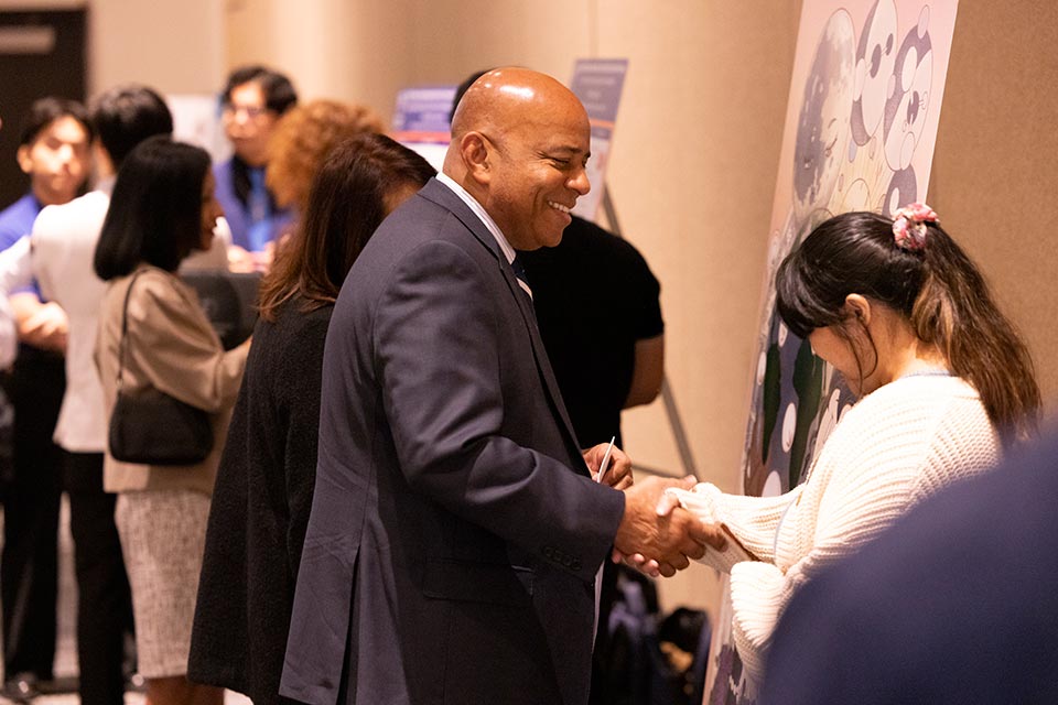 President Rochon shaking hand of student researcher in front of research poster